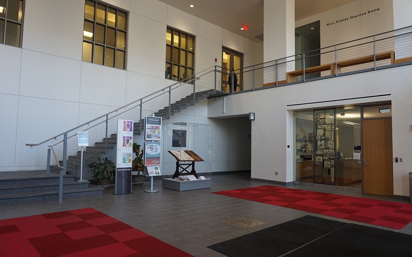Lobby with staircase, display cases and red patterned carpet leading to seminar room