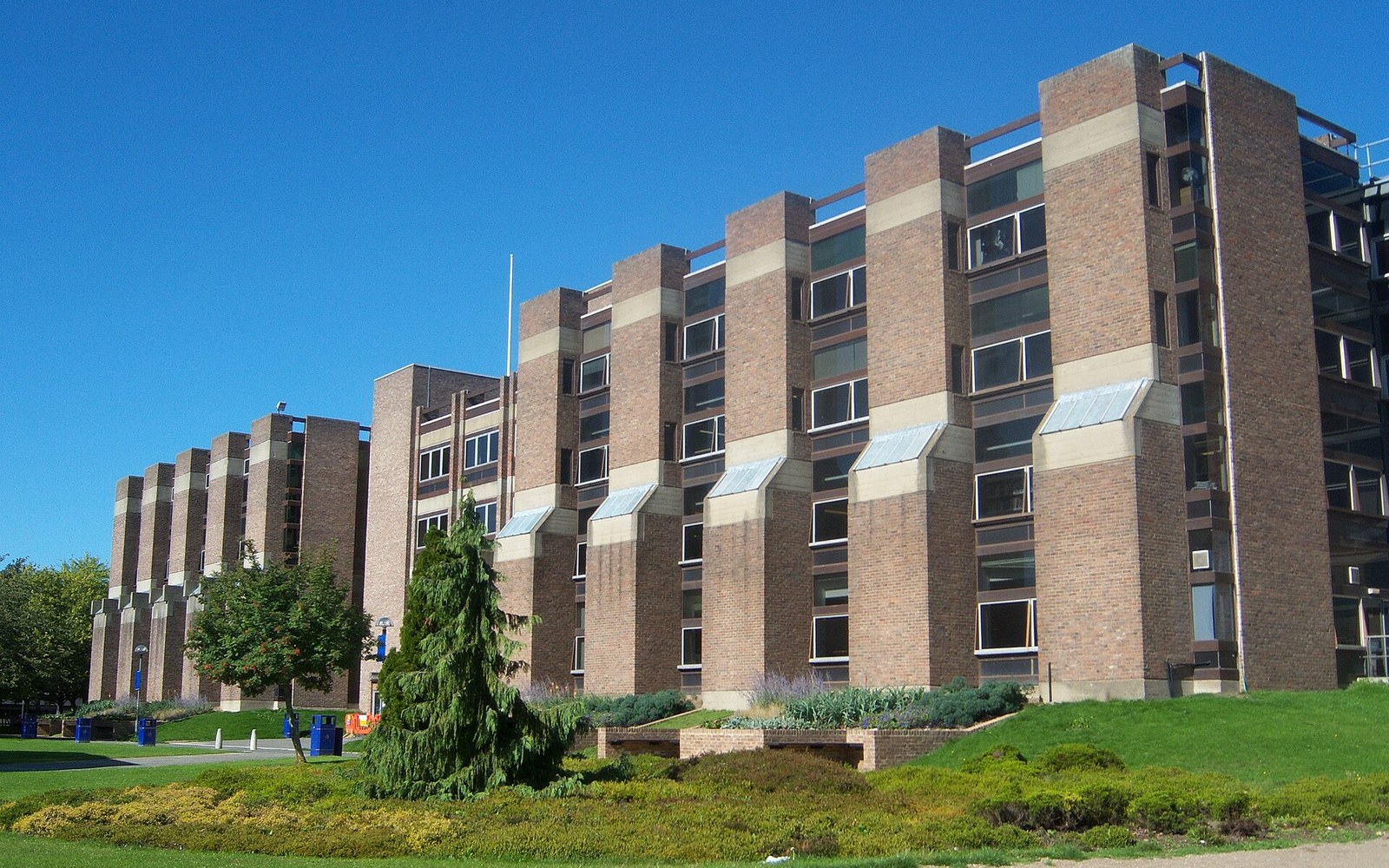 Long brick institutional building with repeating angled bay windows under a clear blue sky