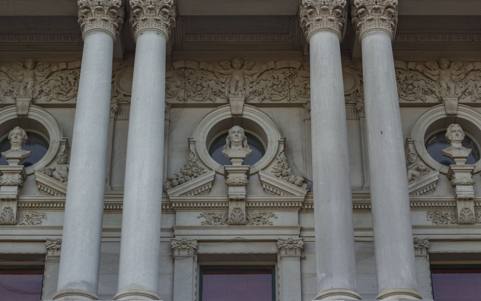 Corinthian columns frame carved busts in circular niches on a stone facade