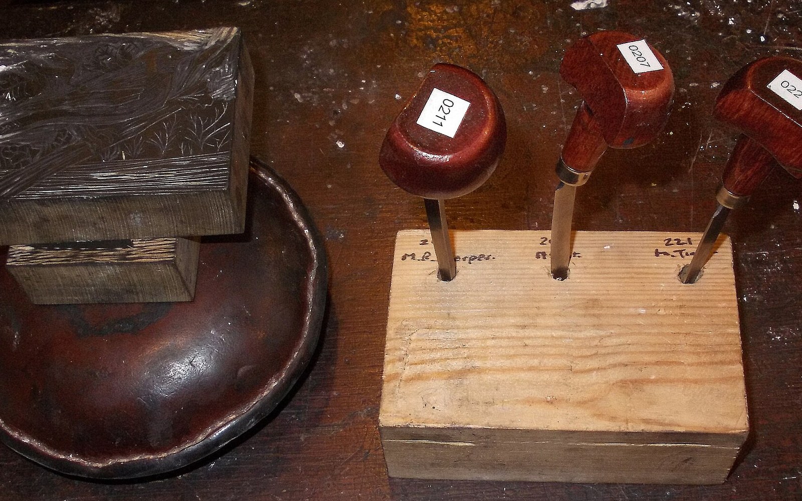 Wood-handled engraving tools with numbered labels stand upright in a wooden block